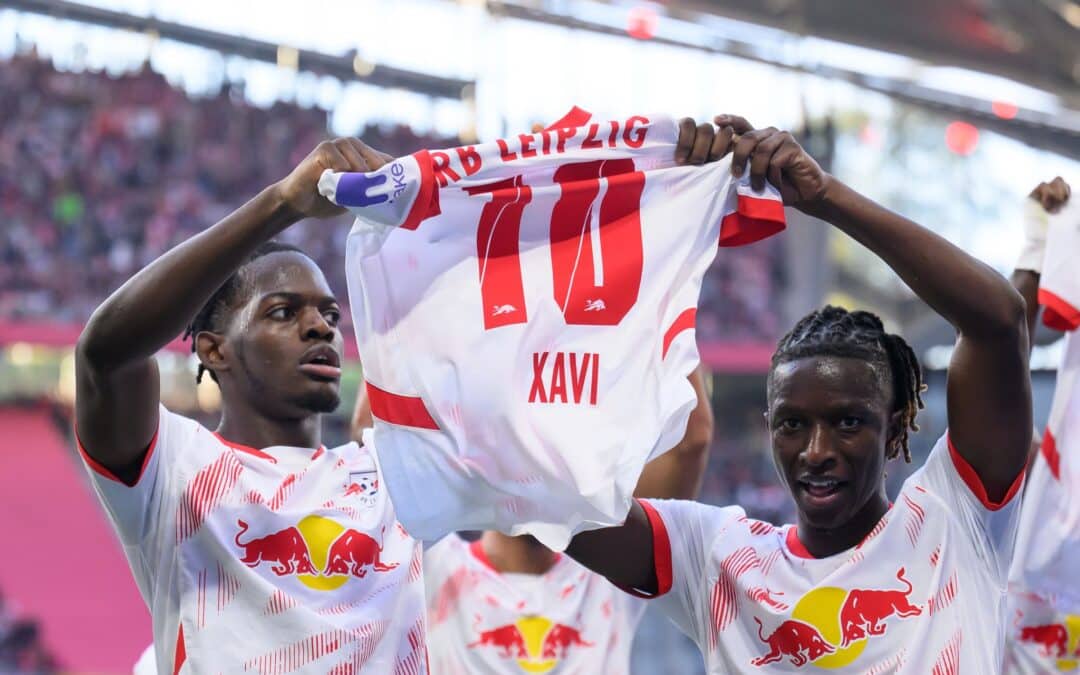 Leipzigs Castello Lukeba (l) und Amadou Haidara halten nach dem 2:1 ein Trikot des verletzten Xavi Simons nach oben.