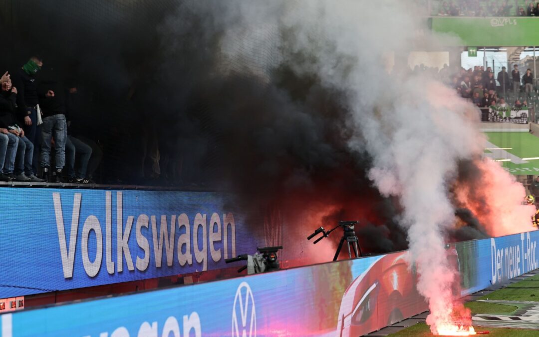 Fans von Wolfsburg werfen Leuchtfackeln auf den Platz.